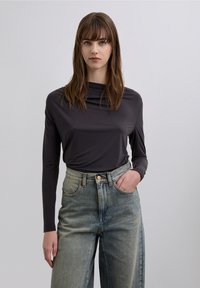 Long-sleeve, dark gray top with a high collar, worn with light blue, high-waisted wide-leg jeans. Smooth fabric and relaxed fit.