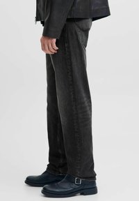 Jeans de denim negro con corte recto, costura visible y superficie texturizada, combinados con botines de cuero azul que presentan un detalle de hebilla.