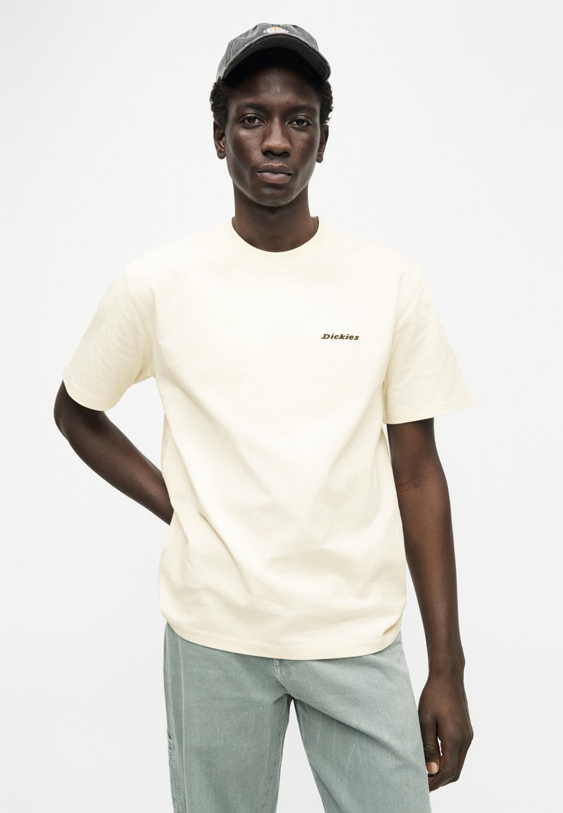 T-shirt in cotone color crema con maniche corte e scollo rotondo, con un piccolo logo nero "Dickies" sul petto a sinistra.