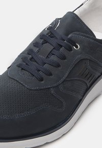 Sneaker in pelle blu navy con design perforato, lacci piatti blu navy, occhielli in argento e suola in gomma bianca con un motivo testurizzato.