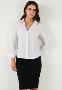 White button-up shirt made of lightweight fabric, featuring a collar, long sleeves, and subtle vertical seams, paired with a black pencil skirt.