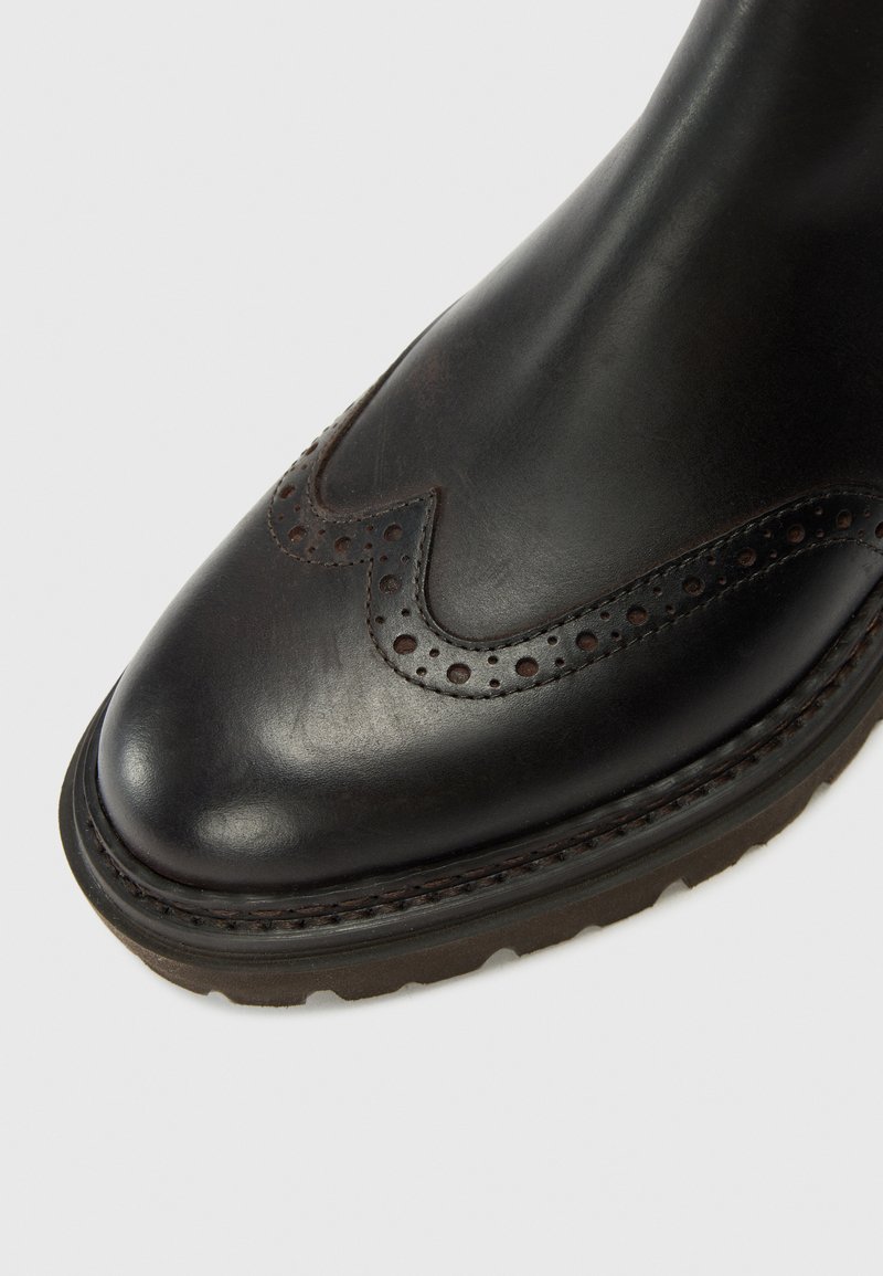 Stivale in pelle nera con finitura liscia, dettaglio di motivo brogue, punta tonda e suola robusta. Caratterizzato da una cucitura a sella per una maggiore durata.