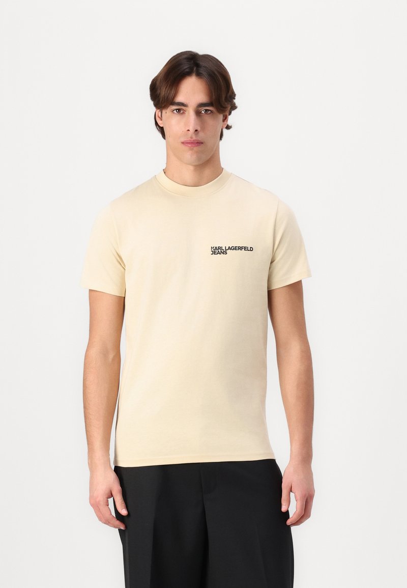 Béžové tričko s krátkým rukávem a kulatým výstřihem. Na levé části hrudi se nachází černé logo "KARL LAGERFELD JEANS". Hladká bavlněná tkanina.