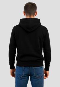 Felpa nera con cappuccio ampio, polsini e orlo a costine. Indossata con jeans di denim blu, mostra un design semplice, casual e di colore uniforme.