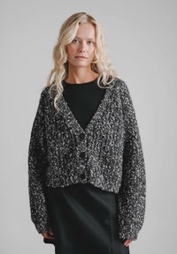 Czarno-biały melanżowy kardigan o fakturowanym splocie, z krótkim krojem, głębokim dekoltem w serek i dużymi czarnymi guzikami.