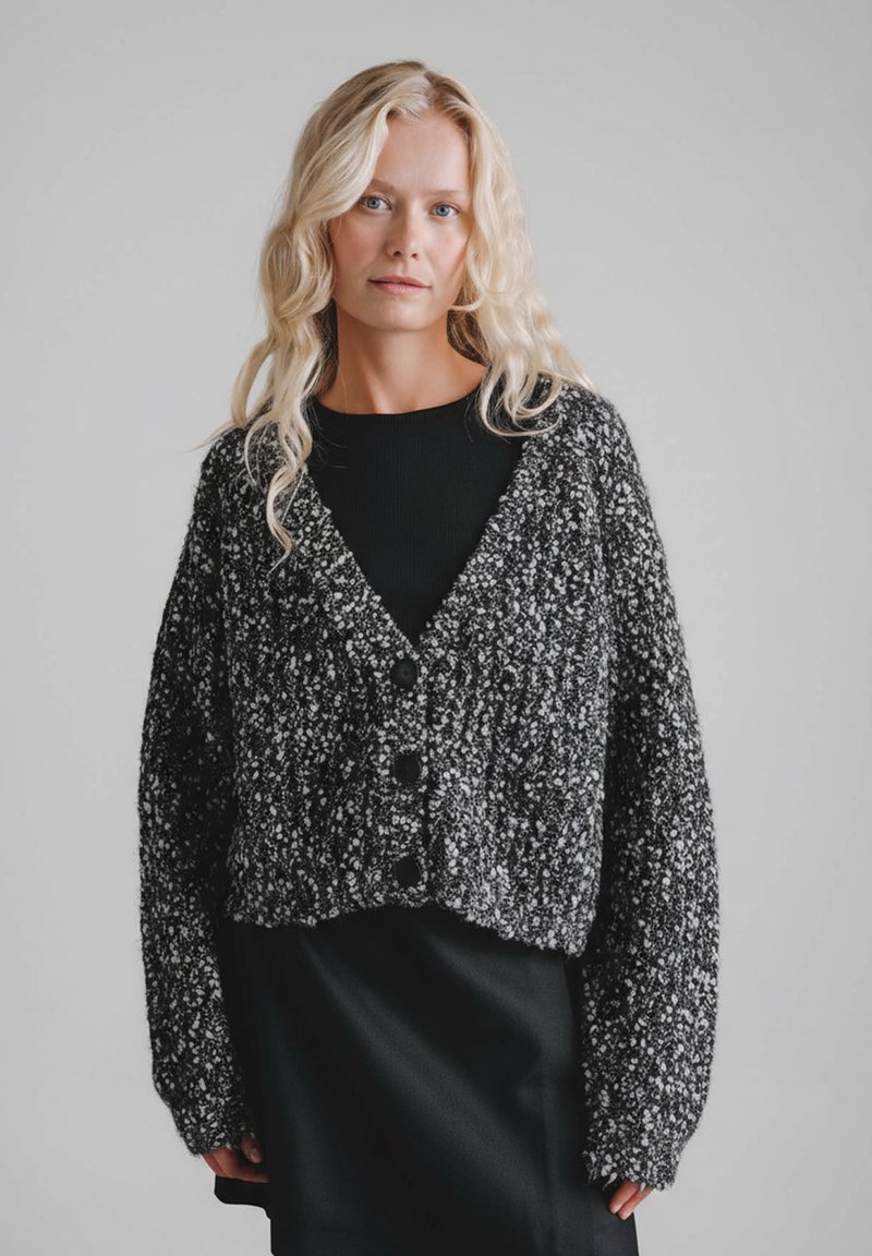 Czarno-biały melanżowy kardigan o fakturowanym splocie, z krótkim krojem, głębokim dekoltem w serek i dużymi czarnymi guzikami.