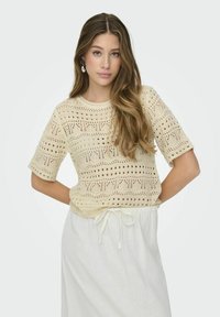 Top de punto color crema con un patrón de encaje texturizado y mangas cortas. Combinado con una falda ligera con cordón en una tela suave.