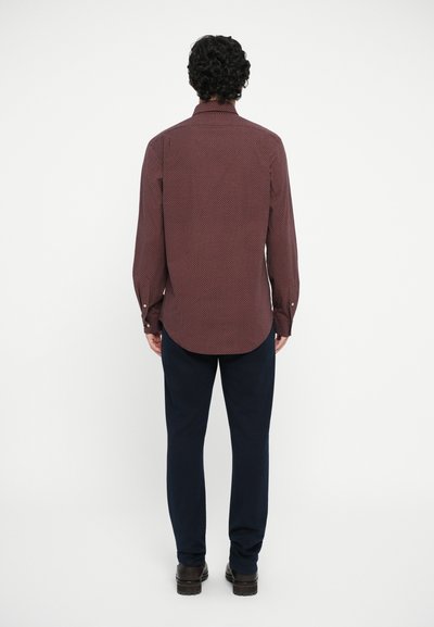 Cămașă maro închis cu mânecă lungă, având un model geometric texturat, asortată cu pantaloni bleumarin. Cămașa are guler și manșete cu nasturi.
