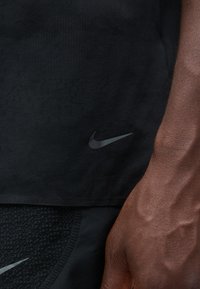T-shirt de sport Nike noir avec un tissu texturé, à manches courtes, et un logo Nike noir bien visible en bas à gauche.