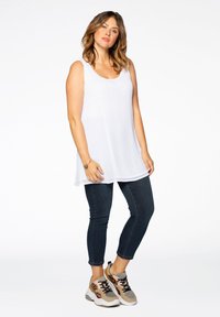 Witte mouwloze top met een ronde hals, gecombineerd met donkerblauwe skinny jeans en sneakers in gemengde kleuren met luipaardaccenten.