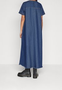 Denim-maksimekko, tummansininen, lyhyet hihat, pyöreä pääntie kolmella napilla, repaleinen helma, yhdistetty mustiin nilkkabootseihin.