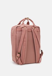 Pink fabric backpack with padded shoulder straps, top handle, and front pocket, featuring textured material and brass accents.