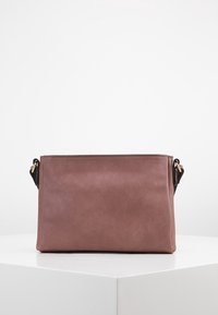 Bolso de cuero mauve rectangular con un acabado suave, con accesorios de correa negra acentuados en dorado, exhibido sobre una superficie blanca contra un fondo liso.