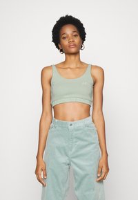 Top cropped verde claro com bainha canelada e bordado discreto, combinado com calças de veludo cotelê verde claro de perna larga com botão à frente.