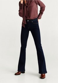 Mørkeblå flagrende jeans med høj talje og fem lommer. Sammen med en mønstret vinrød bluse og brune ankelstøvler.
