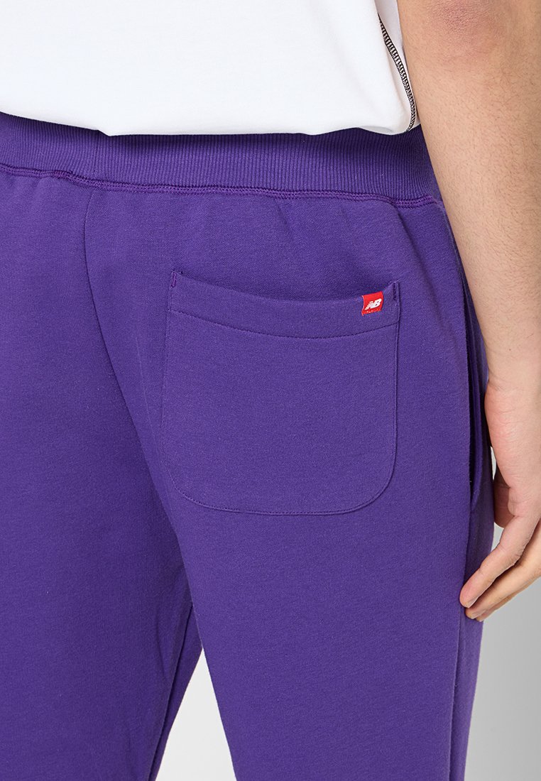 Pantaloni sportivi viola con vita a coste, dotati di una tasca posteriore rettangolare e un piccolo logo rosso. Materiale in cotone morbido.