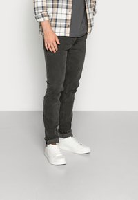 Black stretchy jeans with a slim fit, paired with white sneakers. The top features a button-down plaid shirt in cream, brown, and blue.
