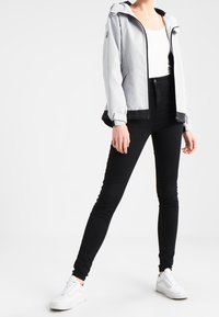 Lys grå hættejakke med sorte accenter, hvid tanktop, sorte skinny jeans og hvide sneakers. Glat tekstur, casual pasform.