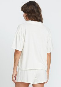 Chemise blanche à manches courtes, ample, avec un col rond et une texture lisse, associée à un short assorti. Design simple sans motifs.