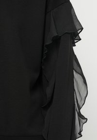 Czarna bluzka z teksturowanej tkaniny, z warstwowym przezroczystym falbaną na rękawie, dodającą głębi i kontrastu do jednolitego wzoru.