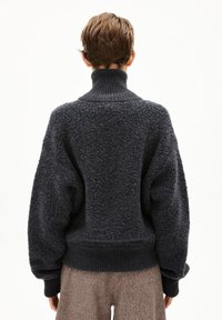 Pull oversized gris foncé avec un col haut côtelé, un tissu texturé et des manches volumineuses. L'ourlet présente une finition côtelée.