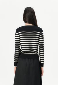 Pull rayé noir et ivoire à manches longues, avec un col et un ourlet côtelés, porté sur une jupe noire. Présente une silhouette ajustée.