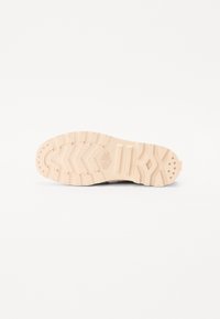 Suela de zapatilla beige claro con un patrón de goma texturizada, que presenta surcos profundos y un detalle en color rosa en el talón.