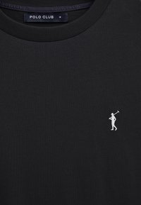 Maglietta nera a girocollo con un piccolo logo di un giocatore di polo ricamato in bianco sul petto e un'etichetta "POLO CLUB" all'interno del colletto, taglia media.