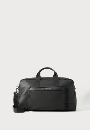 Sac de voyage noir en matériau synthétique lisse. Il dispose de deux poignées et d'une poche zippée à l'avant, avec une bandoulière amovible.