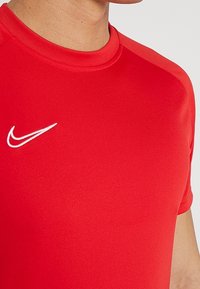 Camiseta deportiva roja de manga corta, hecha de un material suave. Presenta un logo blanco de Nike en el lado izquierdo del pecho. Cuello redondeado.