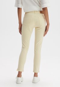 Jean skinny beige clair à texture lisse, avec deux poches arrière et ourlets effilochés, associé à des baskets blanches.