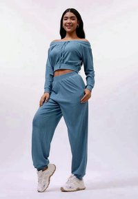 Hellblau geripptes Zweiteiler-Outfit, bestehend aus einem schulterfreien Crop-Top und einer passenden locker sitzenden Hose, kombiniert mit weißen Sneakern.