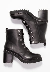 Botas de cuero negras hasta el tobillo con tacones gruesos, cremalleras laterales, cordones en la parte delantera y detalles de tachuelas a lo largo de la suela y el borde superior.