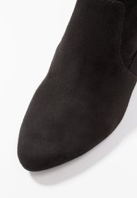 Bottine en daim noir avec un bout pointu et un design épuré, présentant une texture lisse et un détail minimaliste.