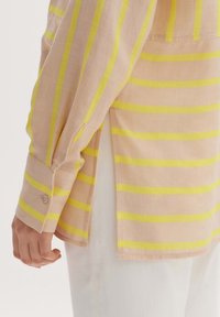 Light pink long-sleeve shirt with yellow vertical stripes, featuring a buttoned cuff and side slits for ease of movement.