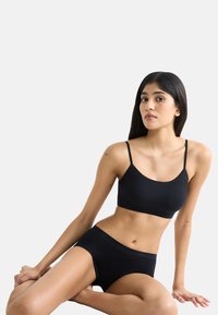 Mustaton sauma-free bralette ohuilla olkaimilla, yhdistettynä samansävyisiin korkeavyötäröisiin alushousuihin. Sujuva pinta, minimalistinen muotoilu, jossa on huomaamaton brändäys vyötärönauhan kohdalla.