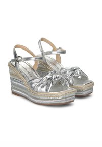 Zilveren metallic wedge sandalen met gedraaide voorkant, verstelbare enkelbandjes en geweven jute details op de zool. Zachte textuur overal.