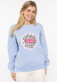 Jasnoniebieska bluza z miękkiego materiału, z okrągłym nadrukiem w panterkę i różowymi sercami. Żebrowane mankiety i pas.