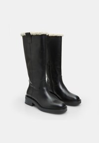 Cizme negre din piele, până la genunchi, cu un guler moale căptușit cu alb, fermoar lateral și toc masiv negru. Textură netedă și design minimalist.