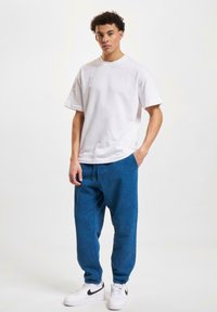 White cotton t-shirt, relaxed fit, paired with blue fleece joggers featuring elastic cuffs and side pockets. White sneakers with black accents.