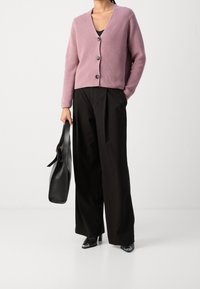 Jasnoróżowy kardigan prążkowany z guzikami, w połączeniu z czarnymi spodniami o szerokich nogawkach i czarną skórzaną torbą. Czarne buty na obcasie z metalicznymi akcentami.