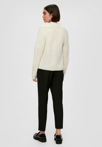 Lichtcrèmekleurige gebreide trui met ribbelstructuur, ronde halslijn en verlaagde schouders, gecombineerd met zwarte tapered broeken en platte zwarte schoenen.