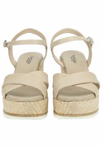 Beige højhælede sandaler med krydsede stropper, flettet jute-platform og ankelrem med metalspænde, der har en glat lædertekstur.
