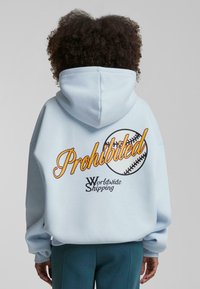 Felpa blu chiaro con una grande grafica "Proibito" e un'illustrazione di baseball sulla schiena. Caratterizzata da un cappuccio con cordini e polsini a coste.