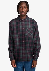 Langsleeve flanellen overhemd in donkerpaars en groene ruit. Voorzien van een button-down kraag, borstzak en knoopsluiting. Zachte textuur.