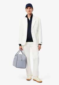 Witte blazer over een marineblauwe zip-up, crèmekleurige broek, gele sneakers; grijze tas met rits en accenten; marineblauwe pet; minimalistische, moderne stijl.