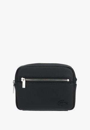 Sac bandoulière rectangulaire noir avec poche zippée à l'avant, tirettes de fermeture éclair argentées et logo crocodile embossé dans le coin inférieur droit.