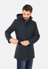 Parka navy con cappuccio, zip frontale, bottoni a pressione e tasche laterali. Realizzata in un materiale liscio e resistente alle intemperie.