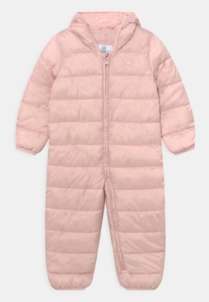 Růžová vycpaná zimní kombinéza s kapucí, vybavená předním zipem, horizontálním prošíváním a elastickými manžetami. Vyrobena z hladkého syntetického materiálu.