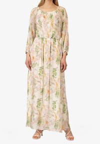 Robe maxi en tissu léger et transparent avec un motif floral dans des tons pastel. Présente des manches longues, un décolleté froncé et une taille à cordon avec des pompons.